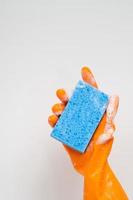 concept de nettoyage, main dans des gants en caoutchouc orange et tenant une éponge bleu clair avec de la mousse pour le nettoyage
