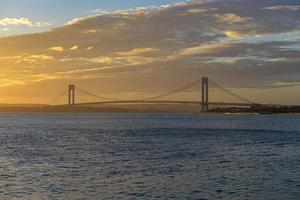 verrazano rétrécit le pont au coucher du soleil depuis brooklyn. le pont un pont suspendu à deux étages qui relie les arrondissements de staten island et de brooklyn à new york city au passage étroit. photo