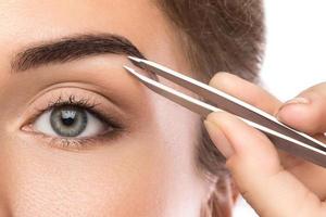 gros plan du visage et des sourcils féminins avec des pincettes photo