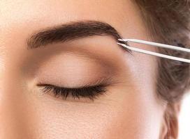 gros plan du visage et des sourcils féminins avec des pincettes photo