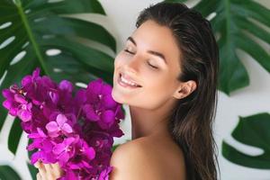 jeune et belle femme avec une peau lisse parfaite tient des fleurs d'orchidées photo