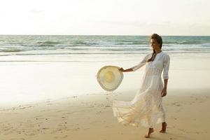 femme vêtue d'une belle robe blanche marche sur la plage au coucher du soleil photo