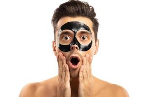 jeune homme avec un masque de charbon de bois noir sur son visage sur fond blanc. photo