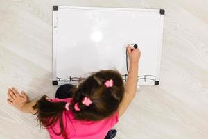 image d'une petite fille heureuse assise près de beaucoup de crayons de couleur sur fond blanc. regardant de côté. photo