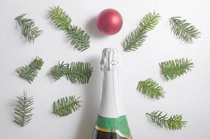 composition de noël.une bouteille de champagne, une boule rouge et de nombreuses branches de sapin sur fond blanc. vue de dessus, flatlay. photo