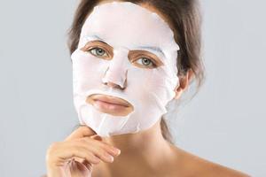 femme avec un masque hydratant en feuille sur son visage isolé sur fond gris photo