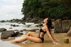 femme assise sur la plage rocheuse avec un cocktail à la noix de coco photo