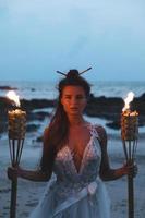 la mariée en belle robe de mariée tient des flambeaux sur la plage photo