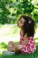 petite fille africaine assise sur une herbe dans un parc de la ville photo