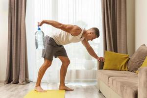 jeune homme athlétique utilisant une grande bouteille d'eau pour l'entraînement à domicile photo