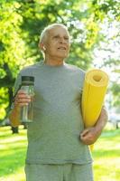 vieil homme actif avec un tapis d'exercice et une bouteille d'eau dans le parc de la ville verte photo
