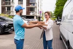 un livreur en uniforme bleu livre une pizza à une cliente photo