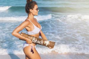 femme sexy portant un maillot de bain avec un vieux panneau d'affichage en bois sur la plage photo