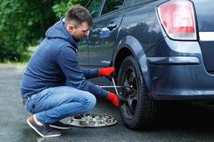 jeune homme changeant de pneu crevé sur sa voiture photo