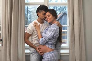 mari et sa femme enceinte dans une étreinte à côté de la fenêtre photo