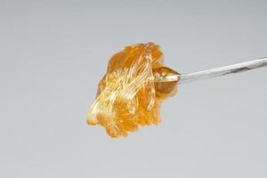 concentré de cire d'extrait de cannabis en or jaune dégoulinant de l'outil de tamponnage en gros plan photo