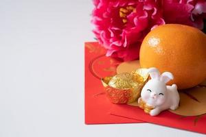 nouvel an chinois du concept du festival du lapin. enveloppes orange, rouges, deux lapins et lingots d'or décorés de fleurs de prunier sur fond blanc. photo