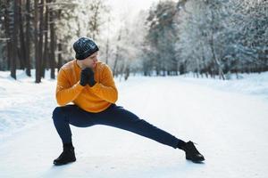 homme athlétique faisant l'échauffement avant son entraînement d'hiver dans un parc enneigé photo