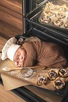 nouveau-né portant une toque de chef est allongé sur le plateau du four avec des muffins photo