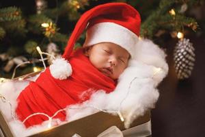 mignon bébé nouveau-né portant un chapeau de père noël dort dans la boîte de cadeau de noël photo