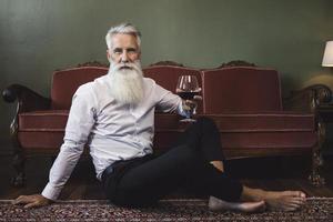 bel homme âgé barbu assis sur le sol et buvant du vin rouge photo