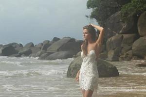 jeune femme vêtue d'une belle robe blanche pose sur la plage photo