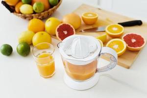 verre de jus d'orange, presse-agrumes et divers agrumes sur la table de la cuisine photo