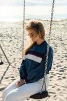 jeune femme souriante assise sur la balançoire à la plage de sable. photo