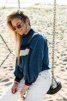 jeune femme souriante assise sur la balançoire à la plage de sable. photo