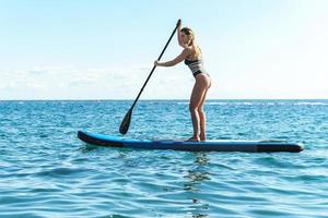 jeune surfeuse en bikini faisant du paddleboard debout dans l'océan. photo