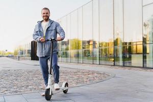 jeune homme joyeux chevauchant son e-scooter dans la rue de la ville photo