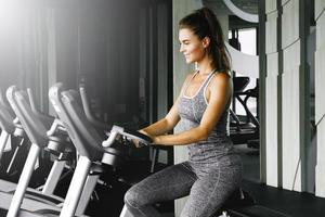 une femme joyeuse fait du vélo sur un vélo stationnaire pendant son entraînement cardio dans la salle de sport photo