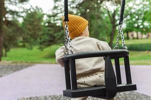 mignon petit garçon assis sur une balançoire dans un parc public photo