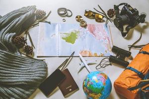 vacances de planification touristique à l'aide de la carte du monde avec d'autres accessoires de voyage autour. smartphone, appareil photo argentique et lunettes de soleil sur fond blanc. sac à dos de voyage