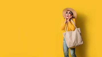 portrait d'une belle fille excitée portant une robe et des lunettes de soleil tenant des sacs à provisions. joyeuse jeune femme avec sac à main sur fond jaune. accro du shopping mode. photo