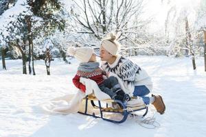 jeune mère et son mignon petit fils avec traîneau rétro dans un parc enneigé pendant la journée ensoleillée photo