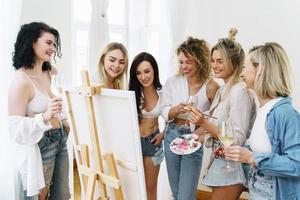 groupe de femmes peignant sur toile et buvant du vin blanc pendant la fête à la maison photo