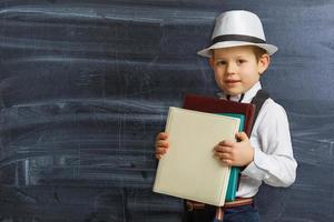 retour à l'école. drôle de petit garçon à lunettes pointant vers le haut sur le tableau noir. enfant de l'école primaire avec livre et sac. éducation. enfant avec un livre photo