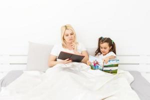 mère et fille au lit en regardant un livre photo