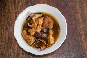 vue de dessus de la nourriture végétarienne chinoise tofu et légumes secs cuits dans la sauce sur un bol en céramique blanche et un fond de table en bois. photo