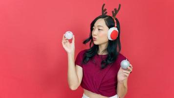 souriante jeune femme asiatique tenant des décorations pour l'arbre de noël sur fond rouge. concept du nouvel an et du jour de noël. photo