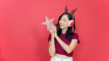 heureuse jeune femme tenant une étoile pour décorer le sapin de noël sur fond rouge. concept du nouvel an et du jour de noël. photo