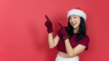 heureuse jeune femme avec bonnet de Noel pointant le doigt sur le côté sur fond rouge. photo