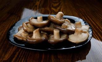 un tas de champignons marinés dans une assiette noire sur une table en bois. nourriture de village saine. champignon de lait noir mariné . photo