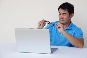 un homme asiatique tient des lunettes pendant qu'il travaille sur un ordinateur portable. concept, problème de vue. optométrie. verres à verres convexes ou concaves. myopie.maladie des yeux photo