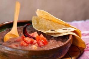 haricots cuits dans un plat d'argile avec tomate et tortillas, plat pauvre mexicain photo