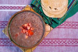 haricots cuits dans un plat d'argile avec tomate et tortillas, plat pauvre mexicain photo