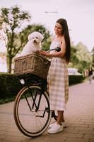 jeune femme avec chien bichon blanc frisé dans le panier de vélo électrique photo