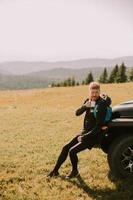 jeune homme se détendre et boire du café par le capot du véhicule tout-terrain à la campagne photo