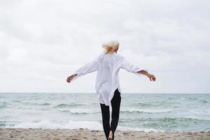 portrait d'une élégante femme blonde en chemise blanche sur une plage de sable à la mer de tempête au vent photo